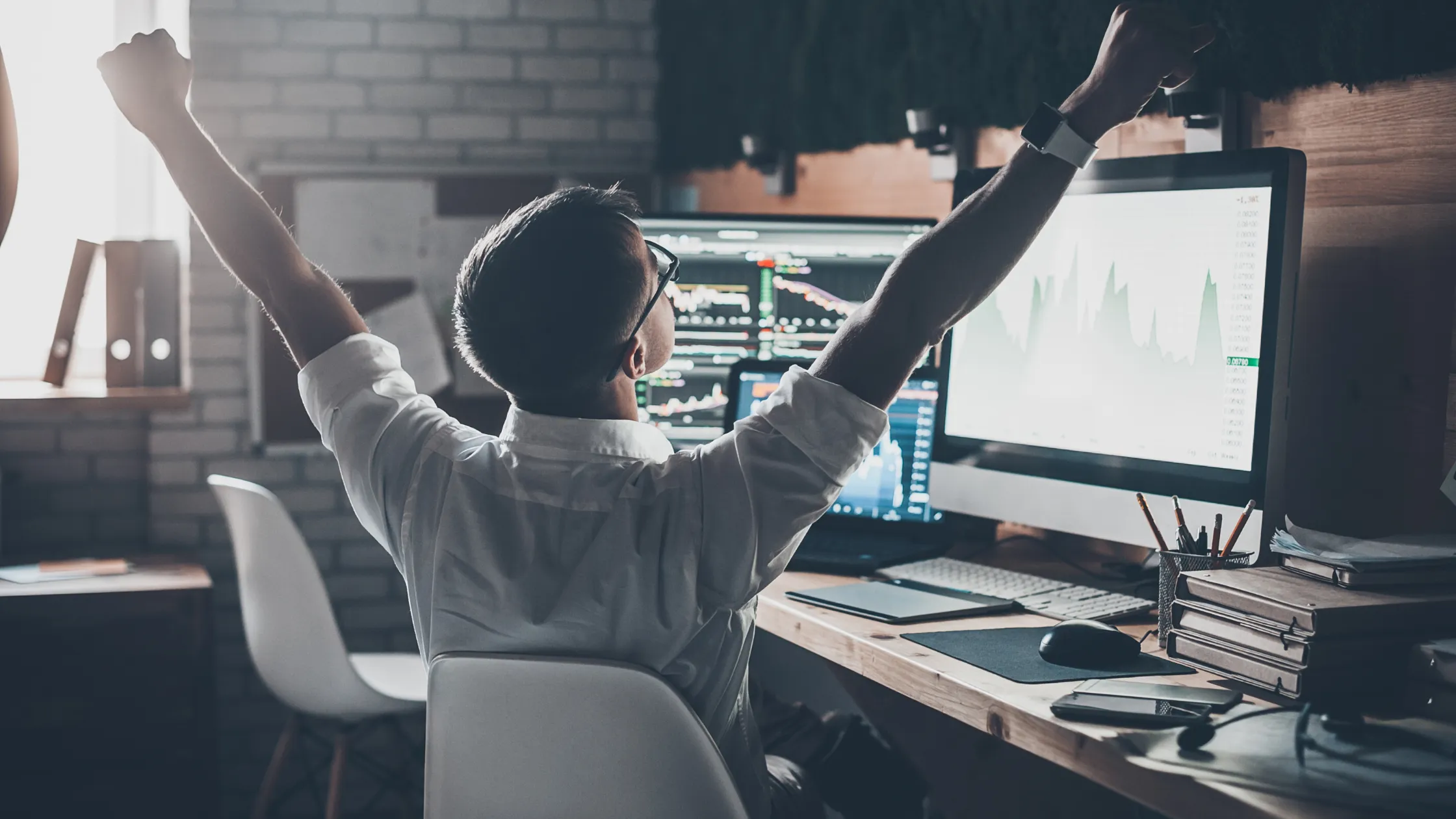 A developer looking at multiple monitors raises his arms in celebration because he isn't managing MLS data on his own.