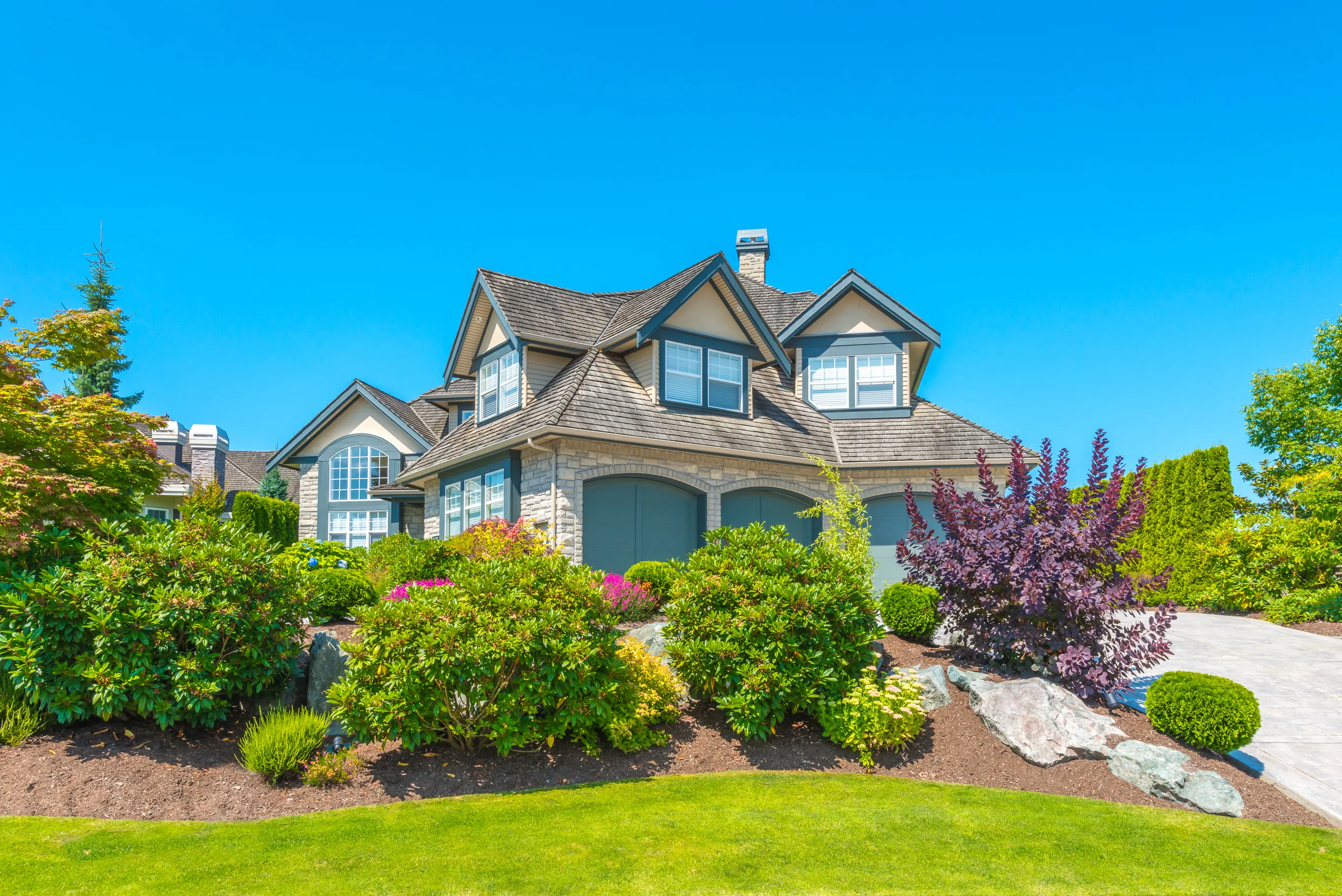 Image of a beautiful large home, with a large, lush, green garden covering the lawn.